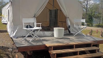 Una gran carpa con dos sillas plegables blancas, una mesa, una terraza de madera y una chimenea de piedra.