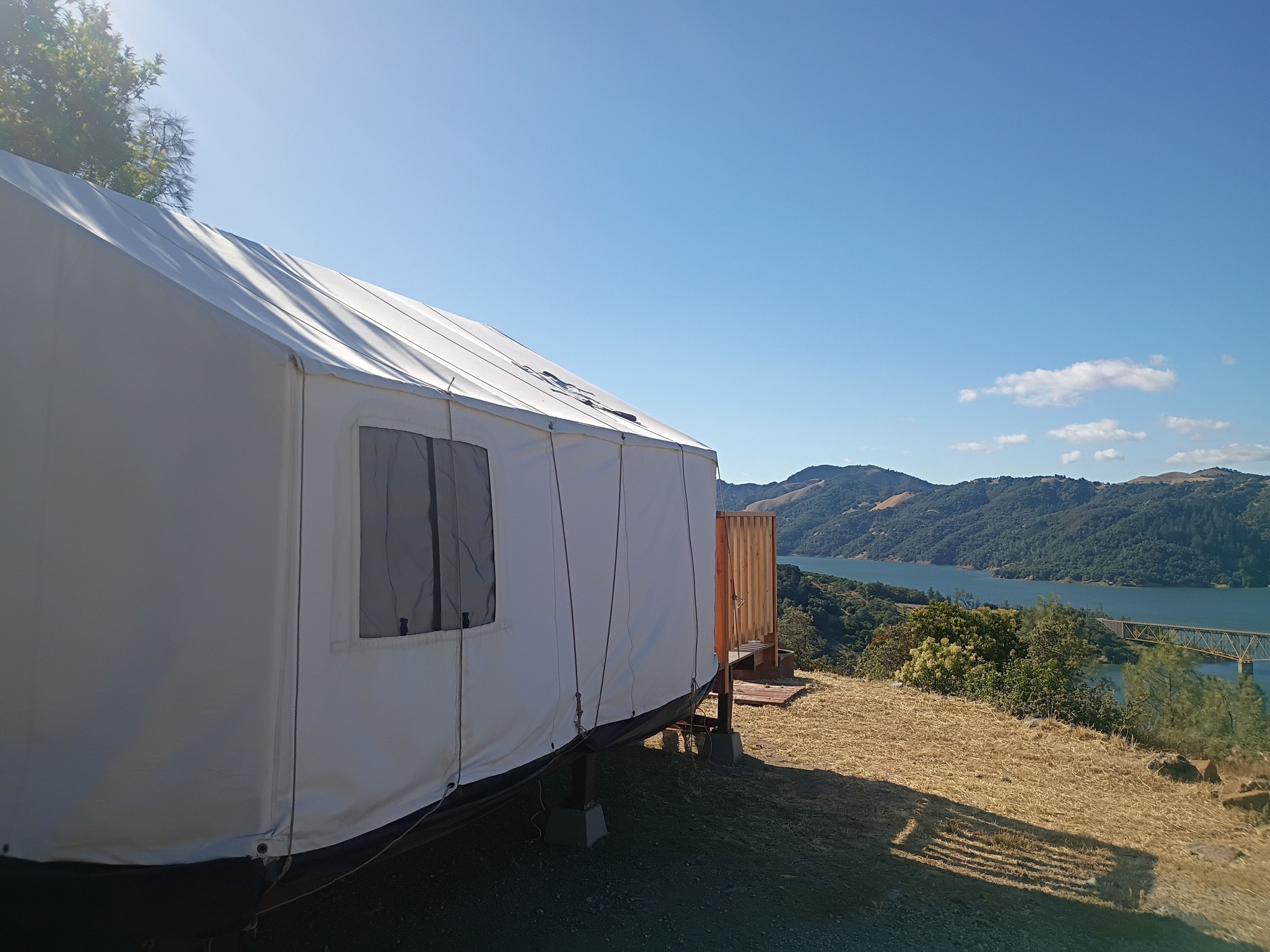 A white tent-like structure with a window, set against a backdrop of a lake and hills.