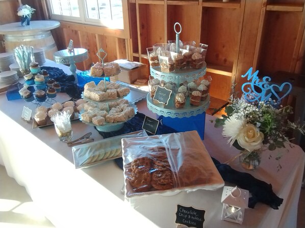 A buffet table with various desserts and snacks, including a tiered cake stand, a sign for 'Carrot Cake', and a 'Chocolate Chip & Taffy Cookies' sign.