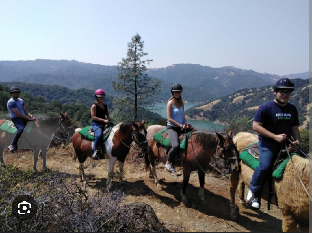 A group of people riding horses on a trail with a scenic view of hills and a lake in the background.