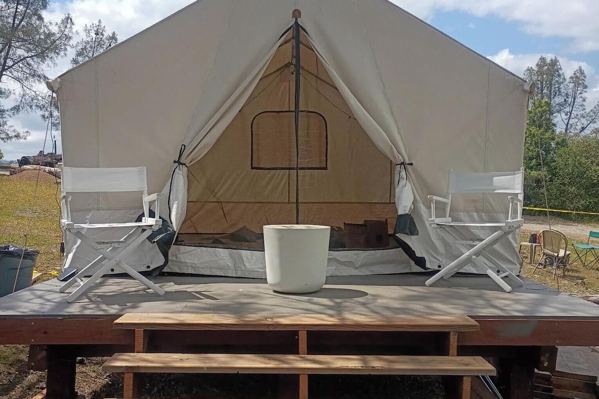 A tent with a central window, a white bucket, and wooden steps leading up to a platform.