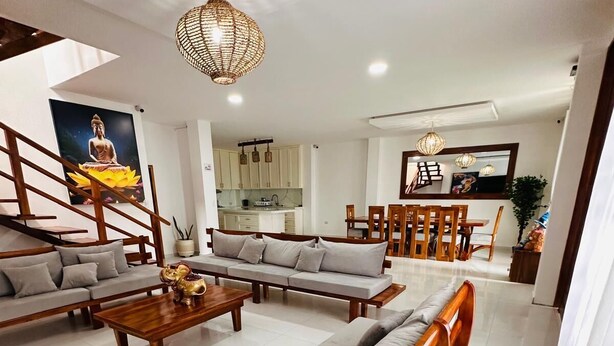 A spacious living area with a sofa set, a coffee table, and a dining table with chairs. There is a staircase with a railing, a kitchen area, and a large window providing natural light. - MONTAÑITA HOUSE Beautiful oceanfront vacation home (Montañita)