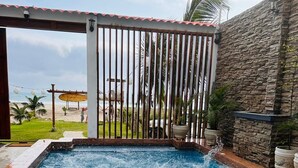 A swimming pool with two people swimming, surrounded by a stone wall and a wooden pergola. - MONTAÑITA HOUSE Beautiful oceanfront vacation home (Montañita)