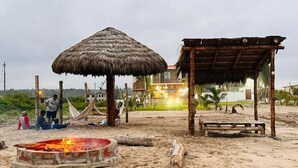 A beach scene with a thatched-roof hut, a wooden structure, and a fire pit. - MONTAÑITA HOUSE Beautiful oceanfront vacation home (Montañita)