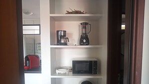A kitchen with a coffee maker, microwave, and kettle on shelves. - Cozy in Calhau near the coast  (Calhau São Luís)