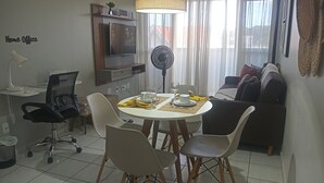 A modern living room with a dining area, a flat-screen TV mounted on the wall, a standing fan, and a sofa. - Cozy in Calhau near the coast  (Calhau São Luís)