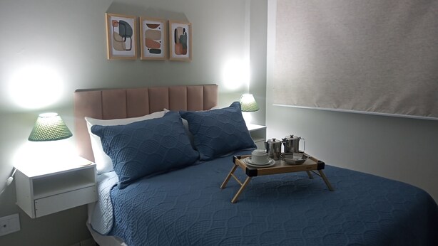 A neatly made bed with a blue quilt, a wooden tray with tea set, and framed artwork on the wall. - Cozy in Calhau near the coast  (Calhau São Luís)
