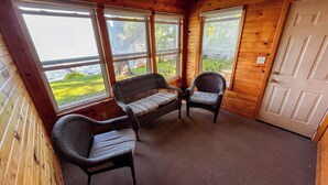 A wooden cabin with a ceiling fan, two wicker chairs, a bench, and a door. - Crow Wing Lakefront Cabin with Stunning Views, Perfect for All Seasons! (Fort Ripley)