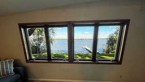 A room with a large window overlooking a lake, a wooden floor, and a blue sofa. - Crow Wing Lakefront Cabin with Stunning Views, Perfect for All Seasons! (Fort Ripley)