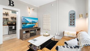 Una sala de estar moderna con una televisión de pantalla plana, un sofá, una mesa de centro y una cocina visible a través de una puerta abierta.