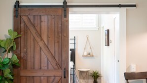 Una rústica puerta corrediza de madera en un cuarto con cama, mesita de noche y lámpara colgante.
