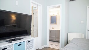 Ein Schlafzimmer mit Bett, Fernseher, Schreibtisch mit Lampe und angrenzendem Badezimmer.