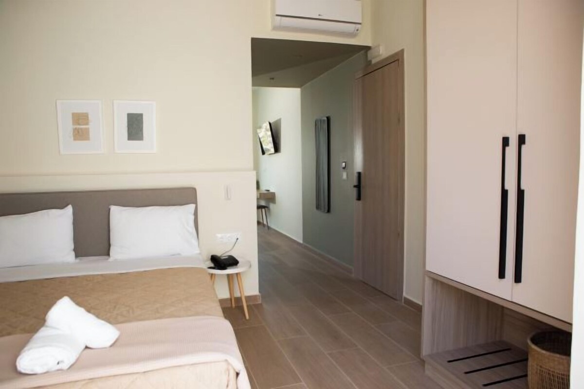 A hotel room with a bed, a small table, a wardrobe, and a hallway leading to another room.