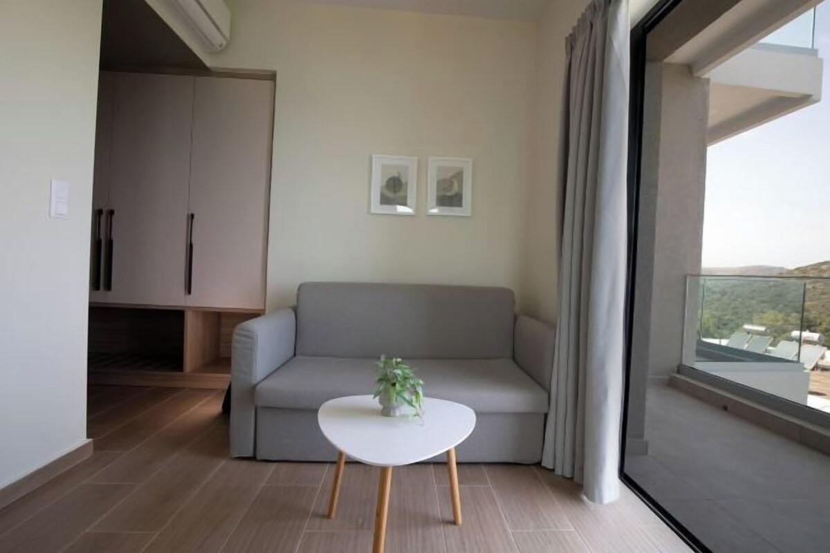 A modern living room with a grey sofa, a small white table with a plant, and a large window with curtains.