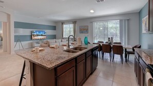 Una cocina moderna con encimeras de granito, una isla central y un comedor con mesa y sillas.