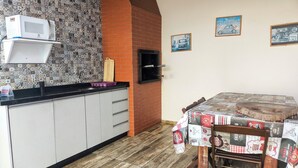 A kitchen with a microwave, a sink, and a table covered with a tablecloth. There are cabinets, a brick wall, and a tiled backsplash. - Hotel e pousada Boulevard Itapoa (Itapoa)