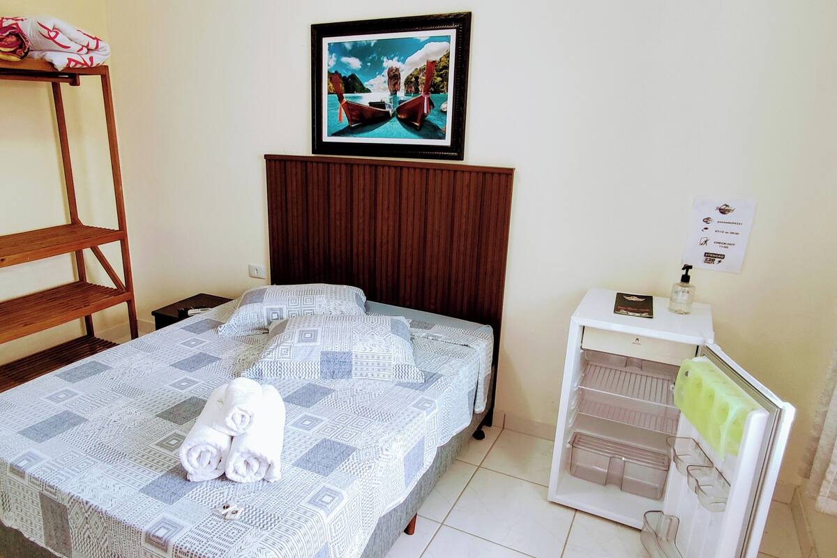 A bedroom with a bed, a wooden shelf, a framed picture, a bedside table, and a small cabinet.
