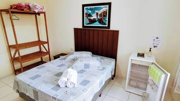 A room with a bed, a wooden shelf, a framed picture, a small cabinet, and a check-out sign.