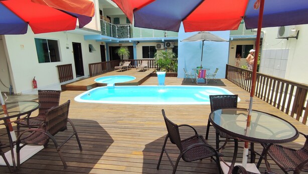 A pool area with wooden decking, lounge chairs, and umbrellas. - Hotel e pousada Boulevard Itapoa (Itapoa)
