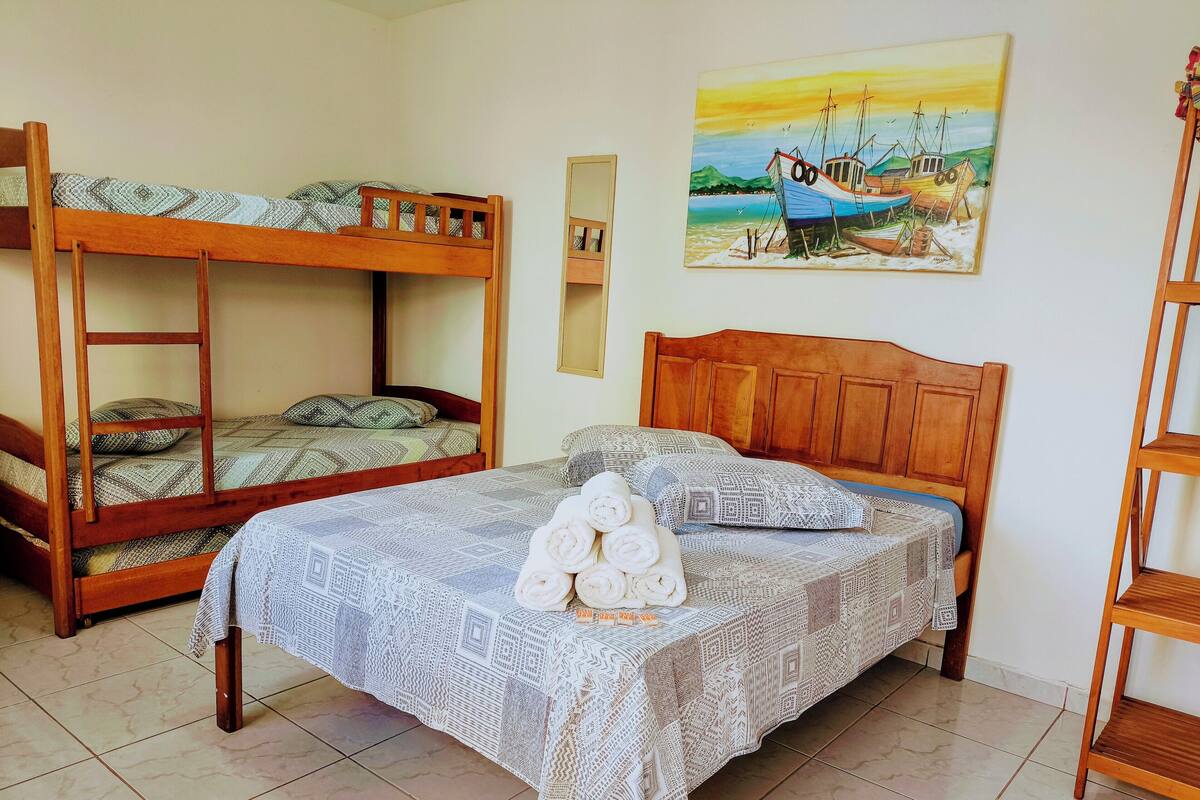 A room with a bunk bed, a single bed with a patterned bedspread, and a painting of boats on the wall.