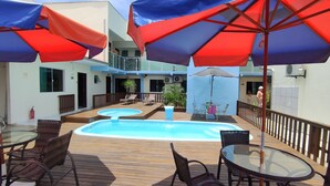 A pool area with multiple lounge chairs and umbrellas, surrounded by a wooden deck and a building with balconies. - Hotel e pousada Boulevard Itapoa (Itapoa)