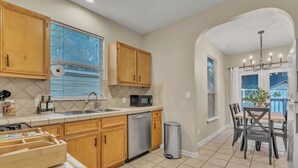 A kitchen with wooden cabinets, a stainless steel dishwasher, a microwave, and a trash can. - Close to Downtown, Close to Airport, Free Parking - Cozy Home in Austin, TX! (Austin)