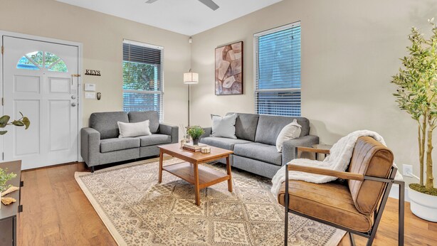 A living room with two grey sofas, a wooden coffee table, a white lamp, and a ceiling fan. - Close to Downtown, Close to Airport, Free Parking - Cozy Home in Austin, TX! (Austin)