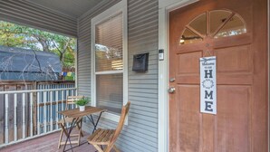 A wooden porch with a table and chairs, a mailbox, and a door with a 'Welcome to Our Home' sign. - Close to Downtown, Close to Airport, Free Parking - Cozy Home in Austin, TX! (Austin)