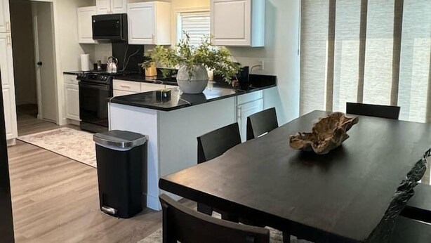 Cocina moderna con armarios blancos, encimera negra y una isla central. Hay una mesa de comedor con sillas y un cuenco decorativo.