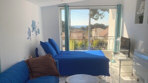 A modern bedroom with two blue beds, a small round table, and a colorful rug. - Studio Bienvenue (Carry-le-Rouet)
