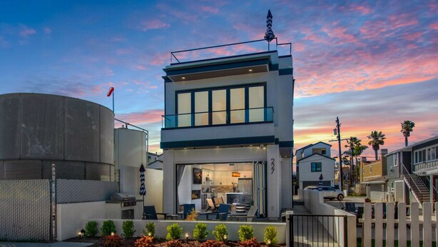 A modern two-story building with a kitchen visible through the front window, a gated driveway, and a clear sky in the background. - Luxury Beachside Villa - Steps to the sand and beach (Huntington Beach)
