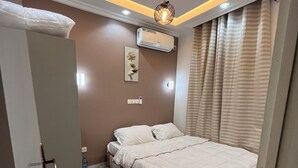 Un dormitorio con cama, puerta, unidad de aire acondicionado e iluminación empotrada en la pared.