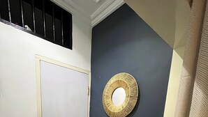 Un baño con una puerta blanca, un espejo redondo, un estante pequeño y un radiador blanco.