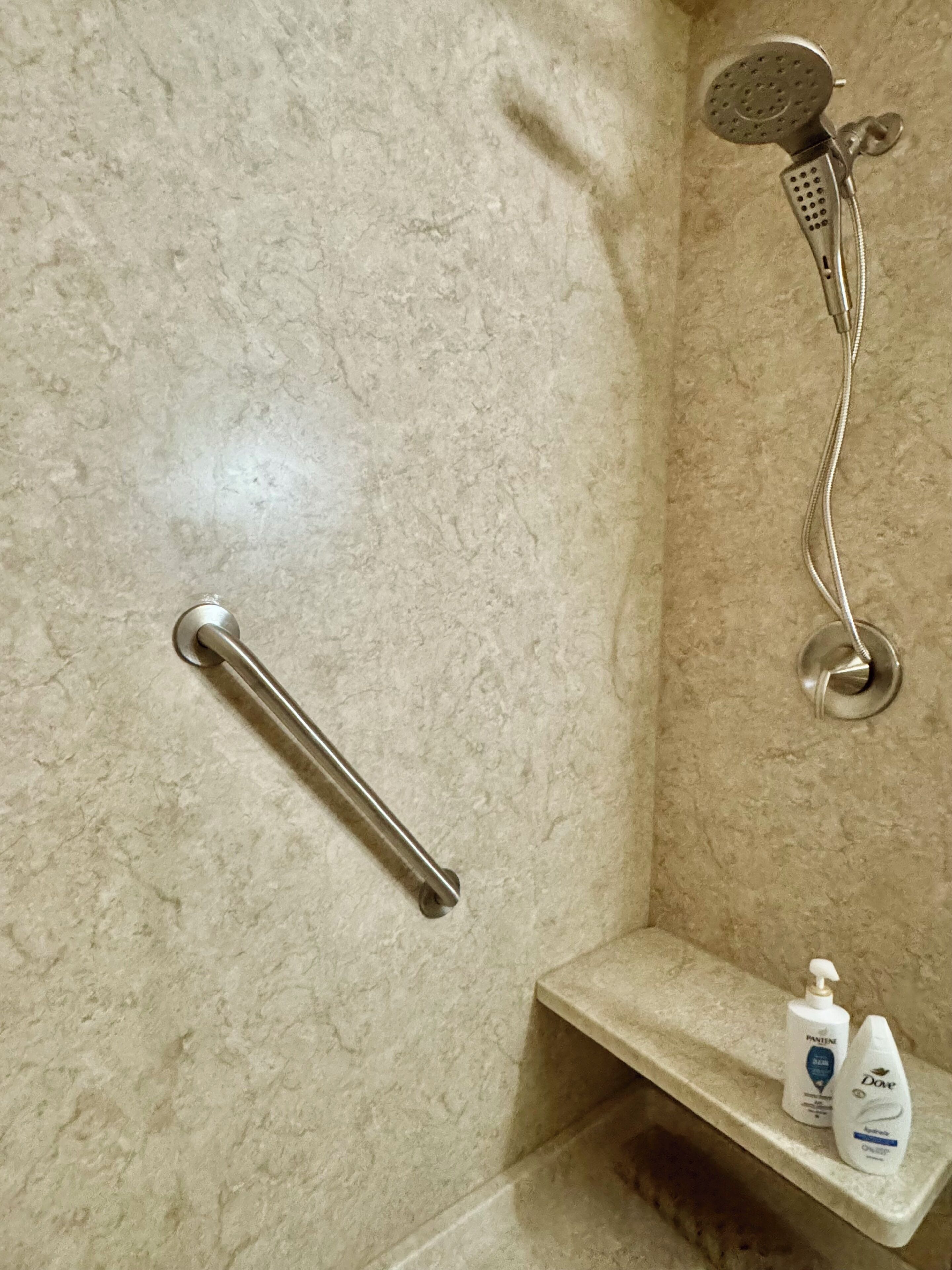 Un baño con ducha, barra de apoyo y estante con artículos de aseo.