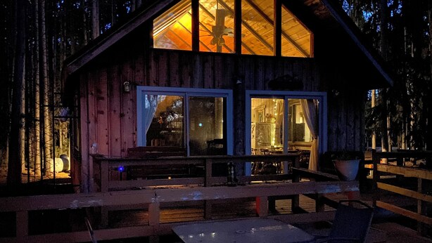 A wooden cabin with large windows, a deck, and outdoor seating.