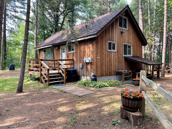A wooden cabin with a porch, a small deck, and a flower planter.