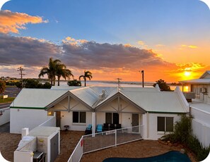 A residential building with a pool, a covered patio, and a view of the sunset over the ocean.