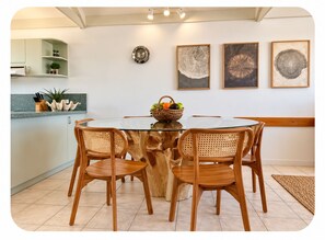 A dining area with a round table surrounded by four wooden chairs, a central woven table base, and a wall-mounted clock.
