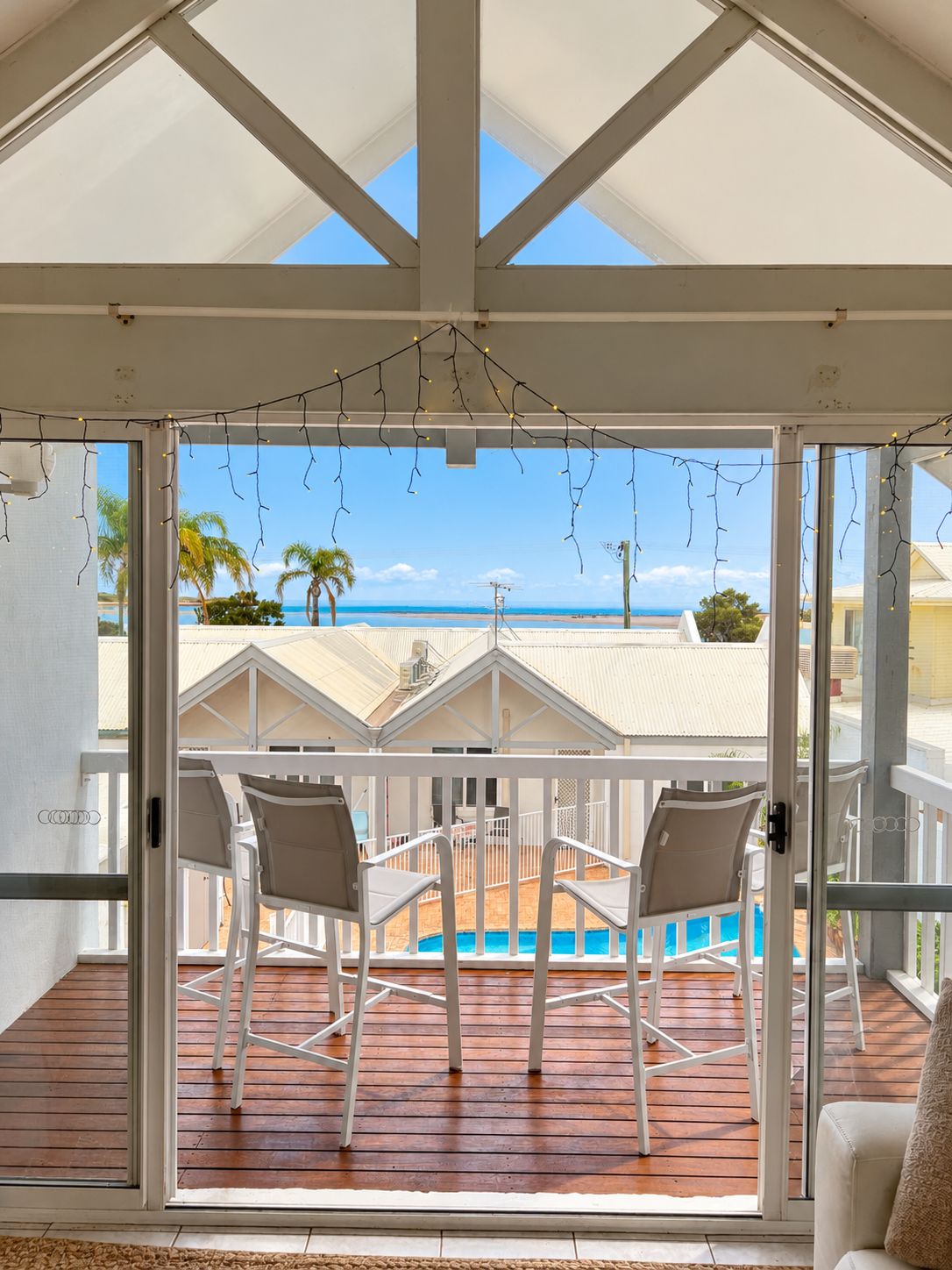 A covered outdoor area with a pool, two chairs, and a view of the beach and ocean.