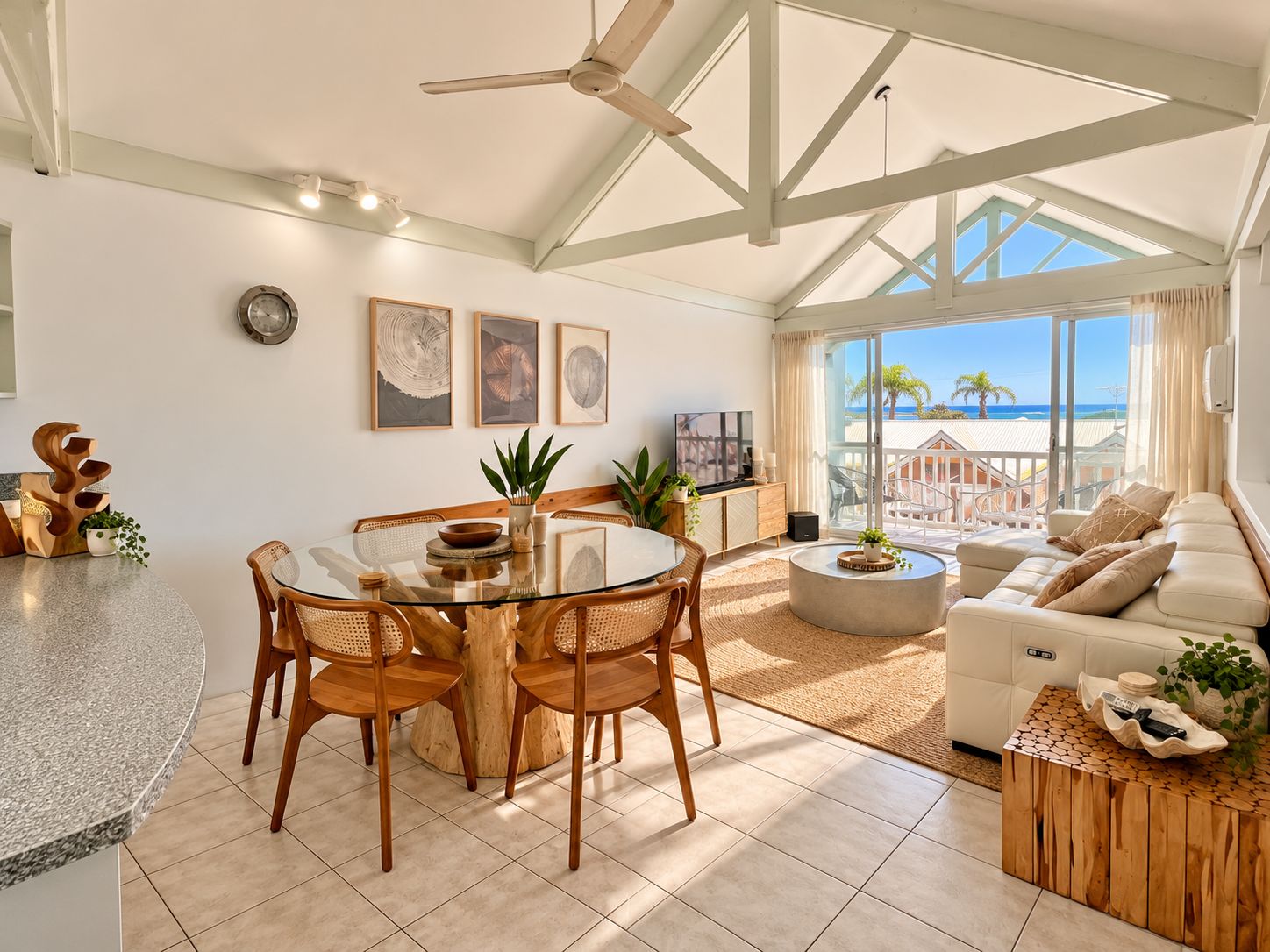 A spacious living area with a glass dining table, comfortable seating, and a view of the beach.