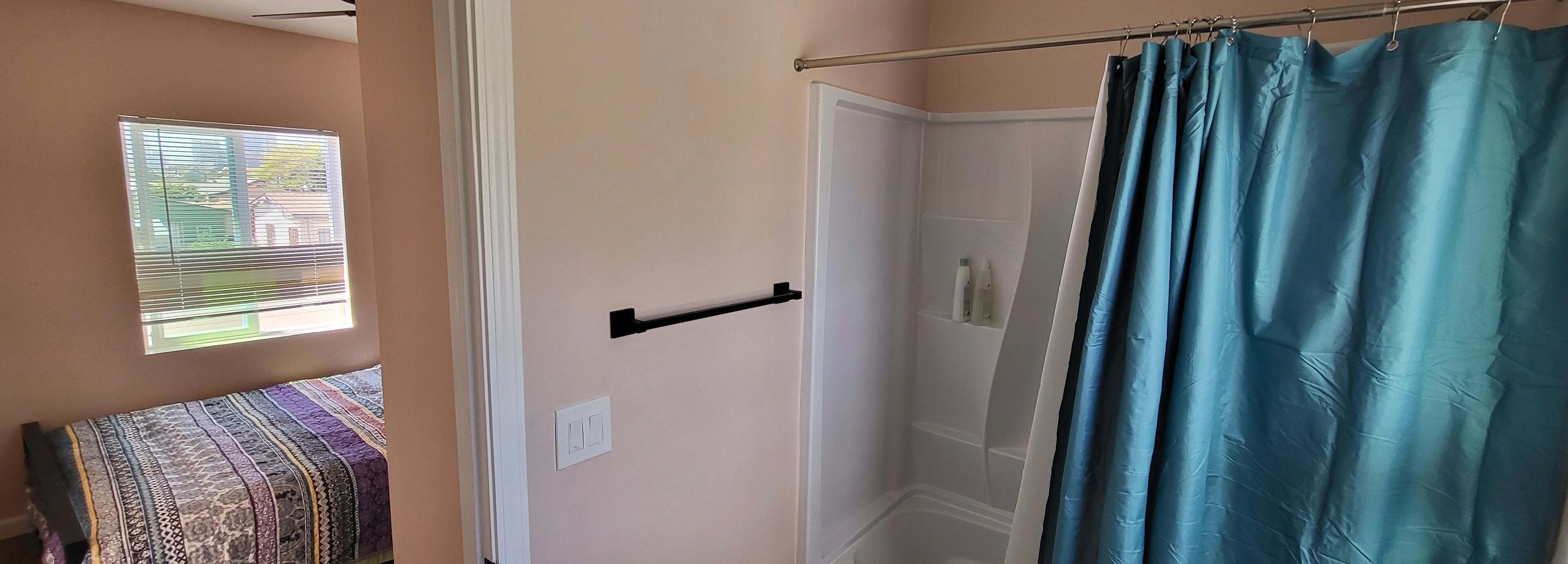 A bathroom with a shower curtain, a towel rack, and a window with blinds.