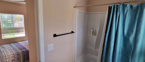 A bathroom with a shower curtain, a towel rack, and a window with blinds.