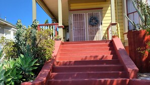 Une maison avec un escalier rouge menant à la porte d’entrée, entourée de cactus et de plantes succulentes.