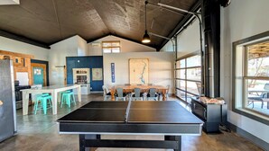 Una habitación amplia con mesa de ping pong, zona de cocina y un gran ventanal que deja entrar mucha luz natural.