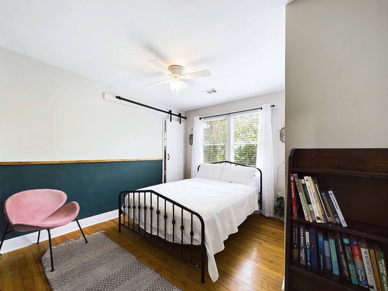 A bedroom with a bed, a chair, a bookshelf, and a window with curtains.