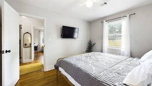 Een slaapkamer met een bed, een plafondventilator, een televisie en een raam met gordijnen.