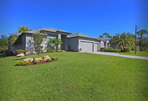 A two-story house with a well-maintained lawn, a driveway, and a small garden with rocks and plants.