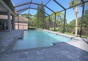 A covered outdoor swimming pool with a clear view of the surrounding trees and a building in the background.
