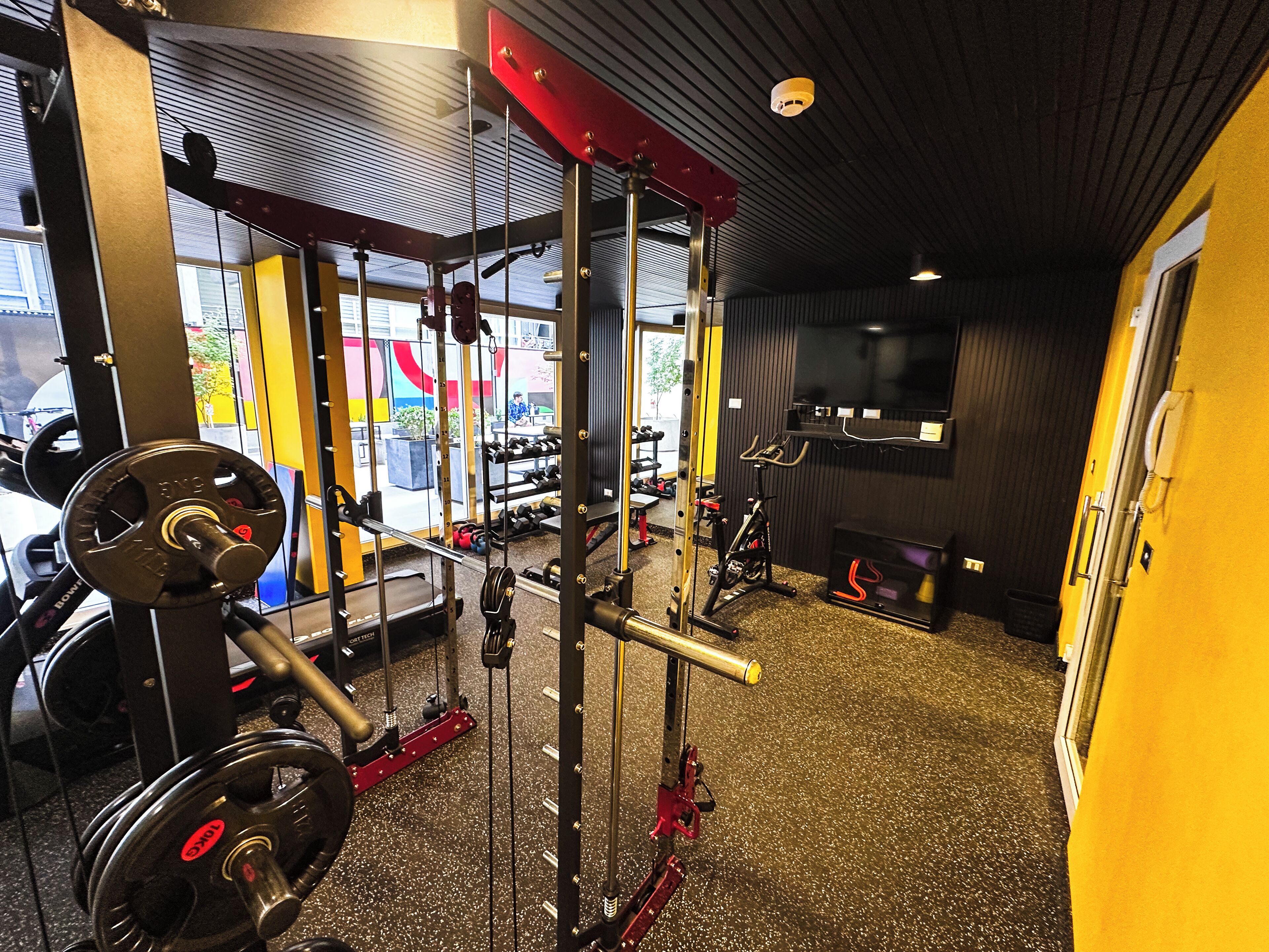 Et fitnessrum med styrketræningsudstyr, løbebånd og et fjernsyn på væggen.