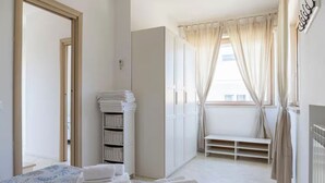 Une chambre d’hôtel avec un lit, une armoire, une fenêtre avec des rideaux et un banc près de la fenêtre.